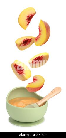 Baby food. Peach slices falling into bowl of puree on white background Stock Photo