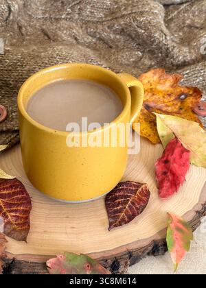 A cozy autumn setup featuring a yellow coffee mug on a rustic wood slice, surrounded by colorful fall leaves and a chunky knit sweater Stock Photo