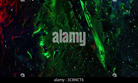 Close-up of wet glass surface with vibrant green and red neon reflections, textured with water droplets and fluid streaks. Stock Photo