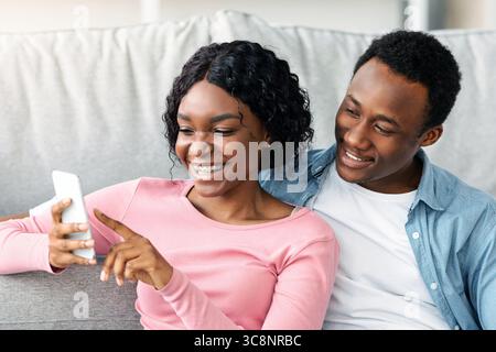 Black lovers with cleaning tools sitting on floor, using smartphone Stock Photo