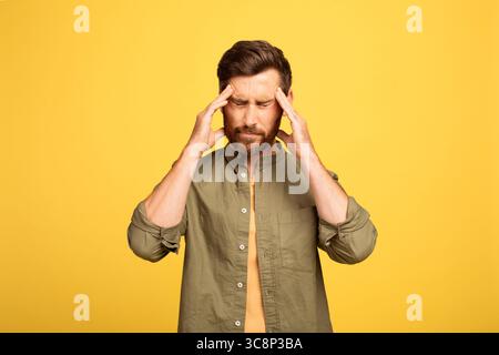Man experiencing stress while standing against a yellow background Stock Photo