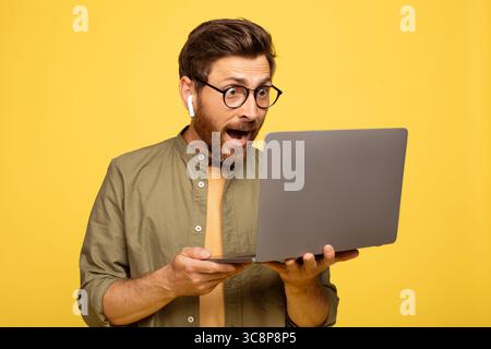 Excited man shows surprise while using laptop in bright yellow background Stock Photo