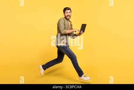 Middle aged man runs while working on his laptop in a bright yellow setting Stock Photo