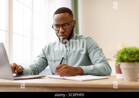 Black Businessman Taking Notes Sitting Working At Workplace In Office Stock Photo