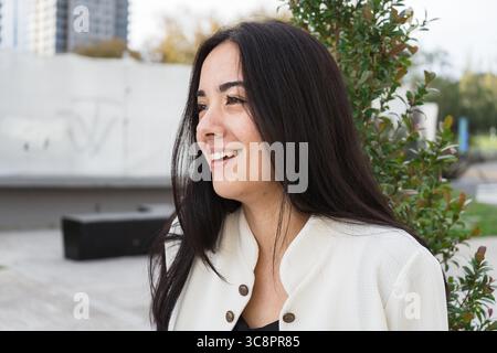 Portrait of a cheerful young latin businesswoman smiling and looking away while standing in a modern city setting Stock Photo