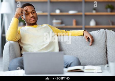 Pensive black businessman sitting on couch in front of laptop Stock Photo