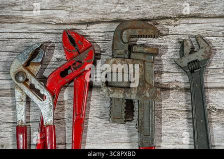 Well-used adjustable wrenches and locking pliers lying on a wooden workbench, showcasing tools of the trade Stock Photo