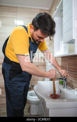 Plumber unclogging sink drain using plunger in bathroom Stock Photo