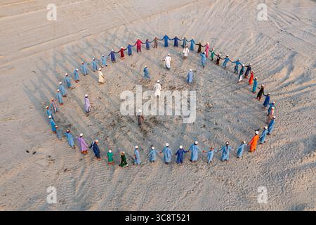 Aerial view of people in a circle holding hands on a sandy field, their colorful robes a stark contrast to the pale earth, Narayanganj, Dhaka Division Stock Photo