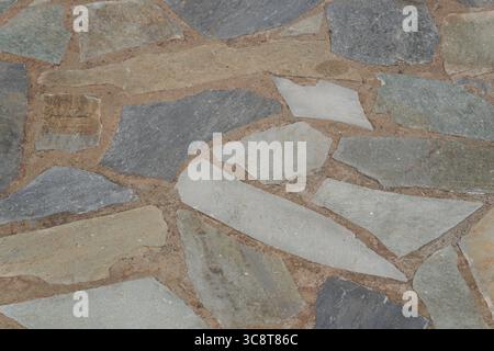 Close-up of an outdoor pavement made with irregular stone tiles in earthy and blue-gray tones, laid in natural patterns. Stock Photo