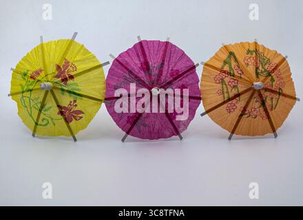Three colorful paper cocktail umbrellas in yellow, pink, and orange arranged side by side on a white background. Stock Photo