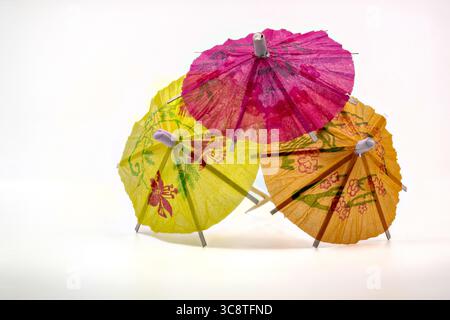 Three vibrant paper cocktail umbrellas in pink, yellow and orange with floral patterns, isolated on white background. Stock Photo