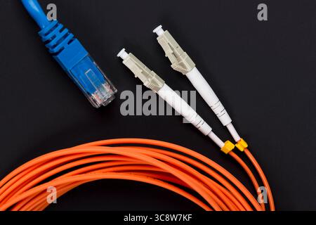 Blue twisted pair patch cord with fiber optics orange cable on dark background. Stock Photo