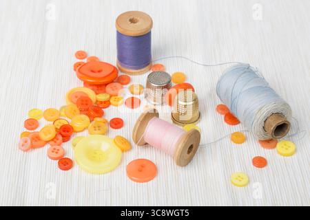 Different thread spools with colorful buttons and thimbles on light surface. Stock Photo