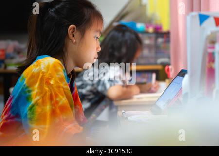 Two Asian schoolgirls studying at home, distance learning and education concept, doing homework together at desk. Stock Photo