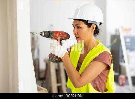 Woman builder using drill to bore hole in wall Stock Photo