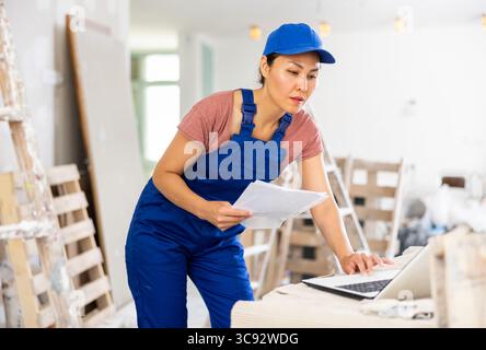 Woman builder checking documentation, using laptop Stock Photo