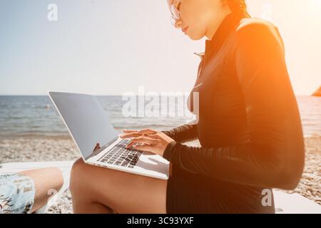 Woman Laptop Beach Work - Woman using a laptop while sitting on a beach. Stock Photo