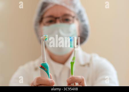 Female dental professional demonstrates two brushing tools electric and manual. A clear message on oral care, helping patients choose wisely for healthier smiles and cleaner teeth. Stock Photo