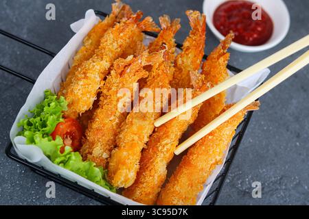 Eating golden-brown Fried Shrimp, or Ebi Fry, stacked in a black wire serving basket lined with white paper. On the side is a bowl of dipping sauce. Stock Photo