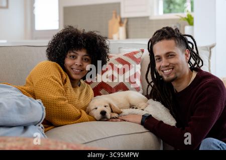 African American couple lying on sofa at home while cuddling sleeping golden retriever puppy Stock Photo