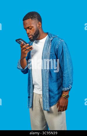Young man using smartphone, recording voice message on blue background Stock Photo