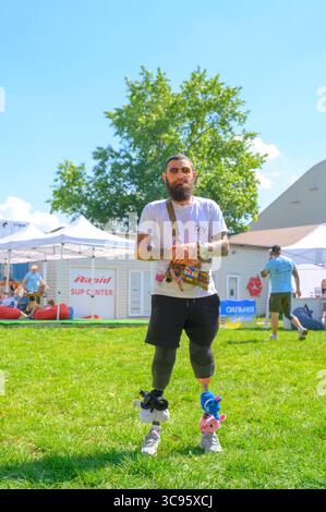 Kyiv, Ukraine - 2d August, 2025: Bearded veteran with prosthetic legs and plush toys attached to them standing on grass during Kyiv INDESTRUCTIBLE veterans' competition, embracing resilience and strength Stock Photo