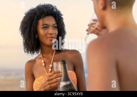 A beautiful young couple enjoys a romantic celebration with champagne in wine glasses on a beach at sunset, celebrating an anniversary or honeymoon va Stock Photo