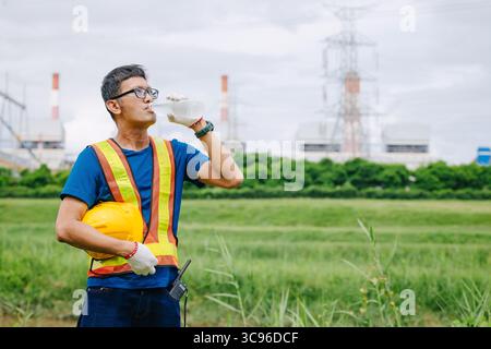Engineer male Asian worker drinking clean water while working outdoor, Thirsty dry refreshing drink brake relax at work Stock Photo