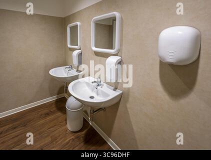 Modern bathroom featuring double sinks with hand soap dispensers and electric hand dryers, characterized by an elegant, minimalist design. Stock Photo