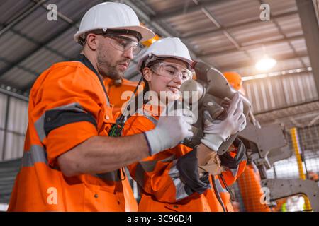 Robotic technician engineer male training helping young women team control operate robot welding arm in modern automated industry factory Stock Photo