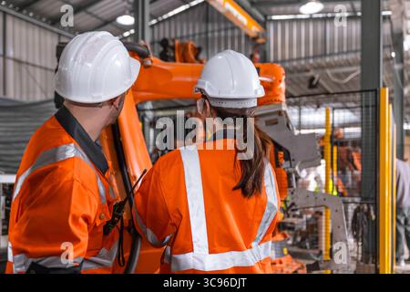 Robotic technician engineer male training helping young women team control operate robot welding arm in modern automated industry factory Stock Photo