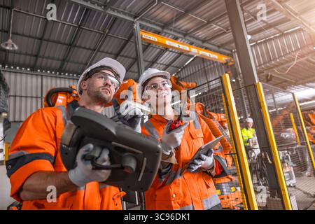 Robotic technician engineer male training helping young women team control operate robot welding arm in modern automated industry factory Stock Photo