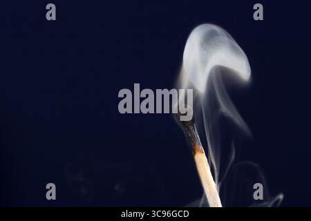 Extinguished match close up with smoke on dark blue background Stock Photo