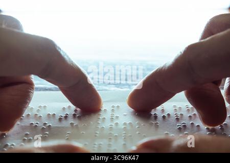 Visually impaired people use their fingertips to read Braille on paper, a tactile writing system. The paper contains dummy Lorem ipsum text. Stock Photo