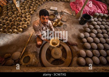 Bogura, Bangladesh - 20 May 2017: View of a potter meticulously shaping clay on a spinning wheel, surrounded by rows of earthen bowls drying in the warm light. Stock Photo