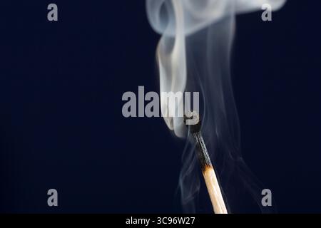 Extinguished match close up with smoke on dark blue background Stock Photo
