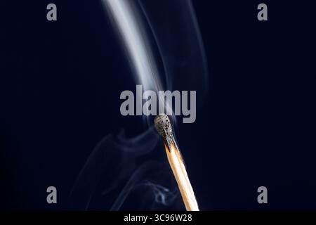 Extinguished match close up with smoke on dark blue background Stock Photo