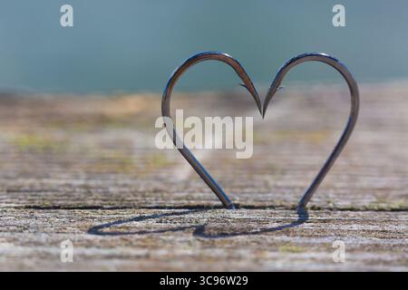 Heart Shape Made of Two Fish Hooks with shadows on wood Stock Photo