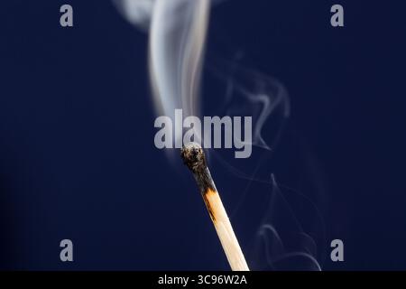 Extinguished match close up with smoke on dark blue background Stock Photo