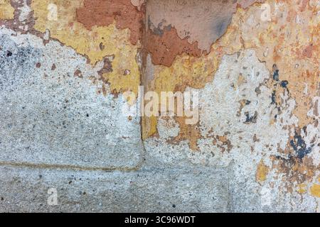 Close-up of weathered wall with peeling paint and texture. The colors include shades of orange, yellow, and gray, creating an abstract aesthetic. Stock Photo