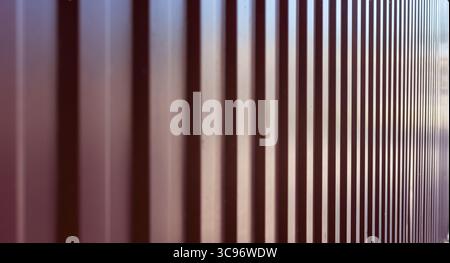 Abstract perspective of a corrugated metal panel fence, showcasing a repetitive linear pattern in a maroon color. Stock Photo