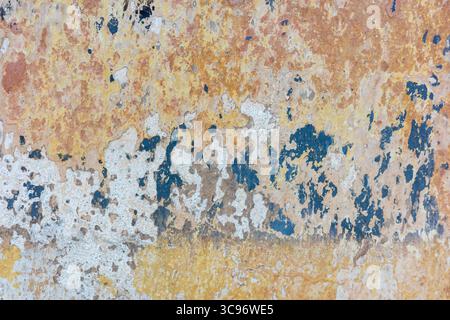 Close-up view of an old, textured wall, showing layers of peeling paint in various colors, creating a weathered, abstract pattern. Stock Photo