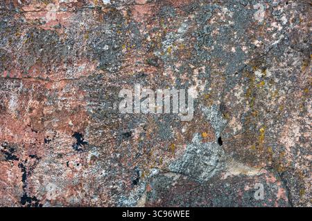 Close-up of a textured stone surface, displaying a variety of colors and patterns. It has an appealing aged and weathered look. Stock Photo