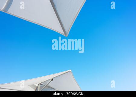 A bright blue sky frames white parasols, offering a cool contrast. The composition emphasizes simplicity, perfect for summer. Stock Photo