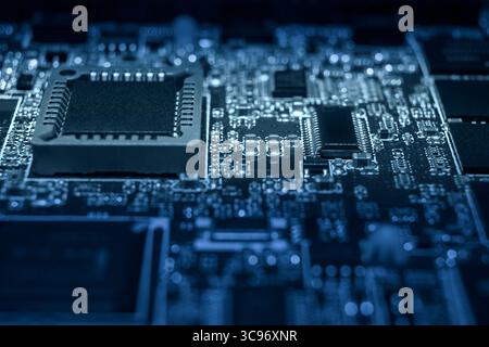 Intricate circuit board features various microchips and electronic components illuminated in blue light, showcasing advanced technology. Stock Photo