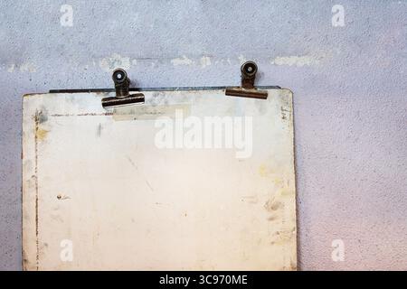 Old worn drawing board with two rusty metal binder clips, mounted against a faded pastel textured wall. Stock Photo