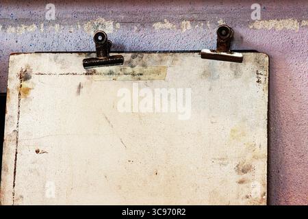 Detailed closeup view of the upper part of an old drawing or sketch board featuring rusty metal clips against a textured purple wall Stock Photo