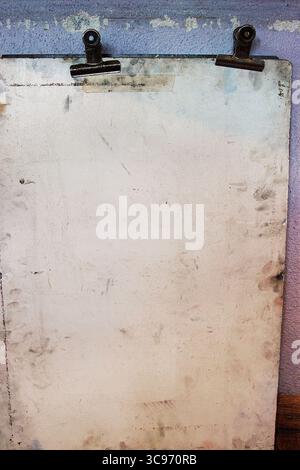 Old worn drawing board with two rusty metal binder clips, mounted against a faded pastel textured wall. Stock Photo