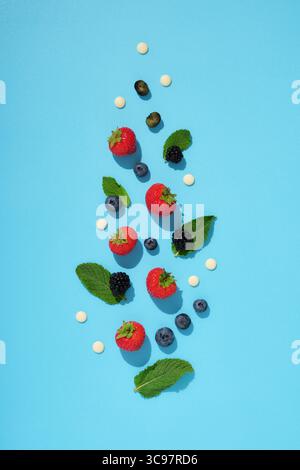 Scattered fresh berries, mint leaves, and white chocolate drops on a bright blue background. Healthy summer ingredients. Stock Photo
